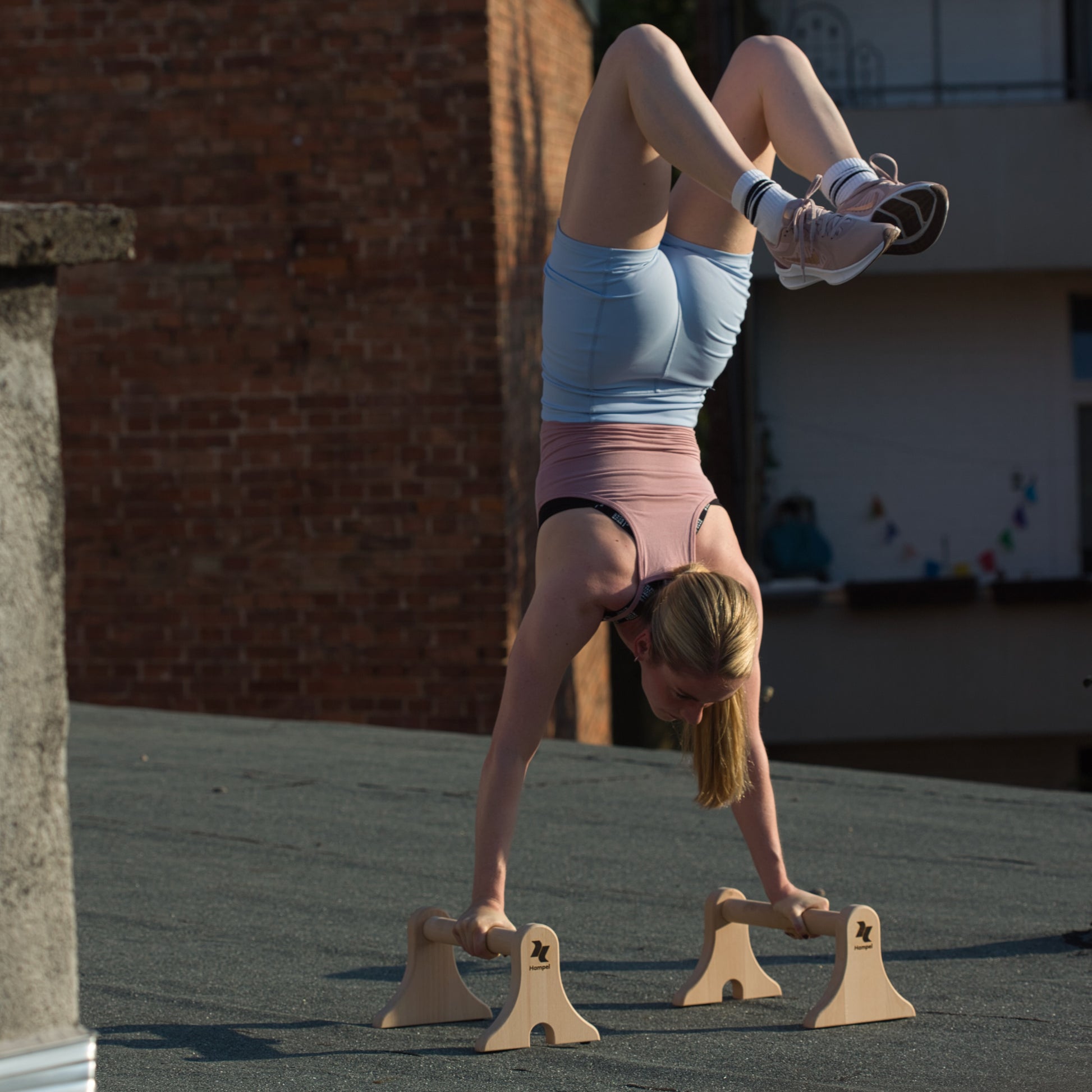 sportliche-frau-macht-handstand-auf-liegestuetzgriffen-maxibars-auf-einem-flachdach